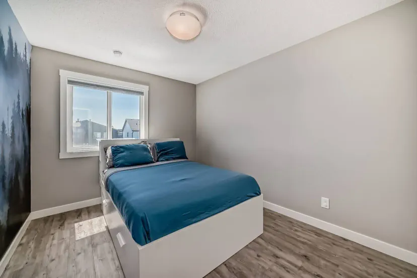 Acogedor dormitorio con una cama queen, gran ventana y decoración moderna con ropa de cama azul suave y suelo de madera