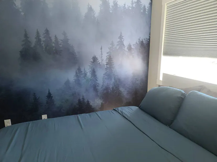 Gemütliches Schlafzimmer mit einer blauen Bettdecke und einer waldthemen Akzentwand mit nebligen Bäumen