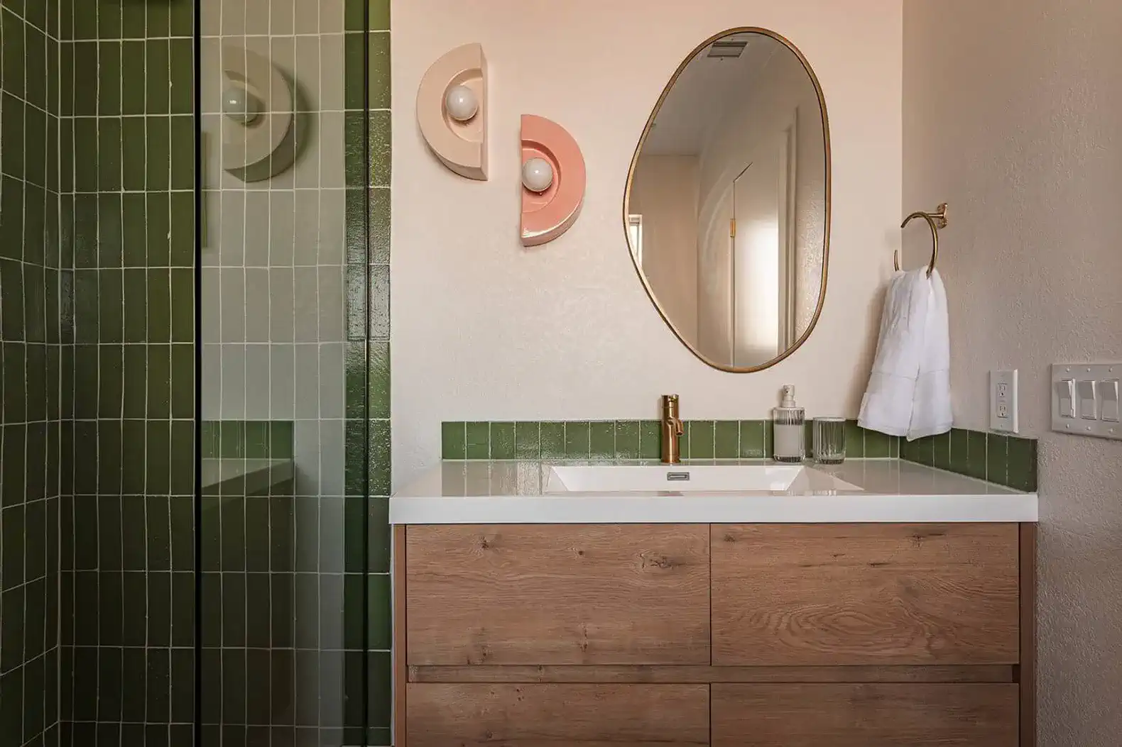 Modern bathroom featuring green tiles, a round mirror, and wooden cabinetry