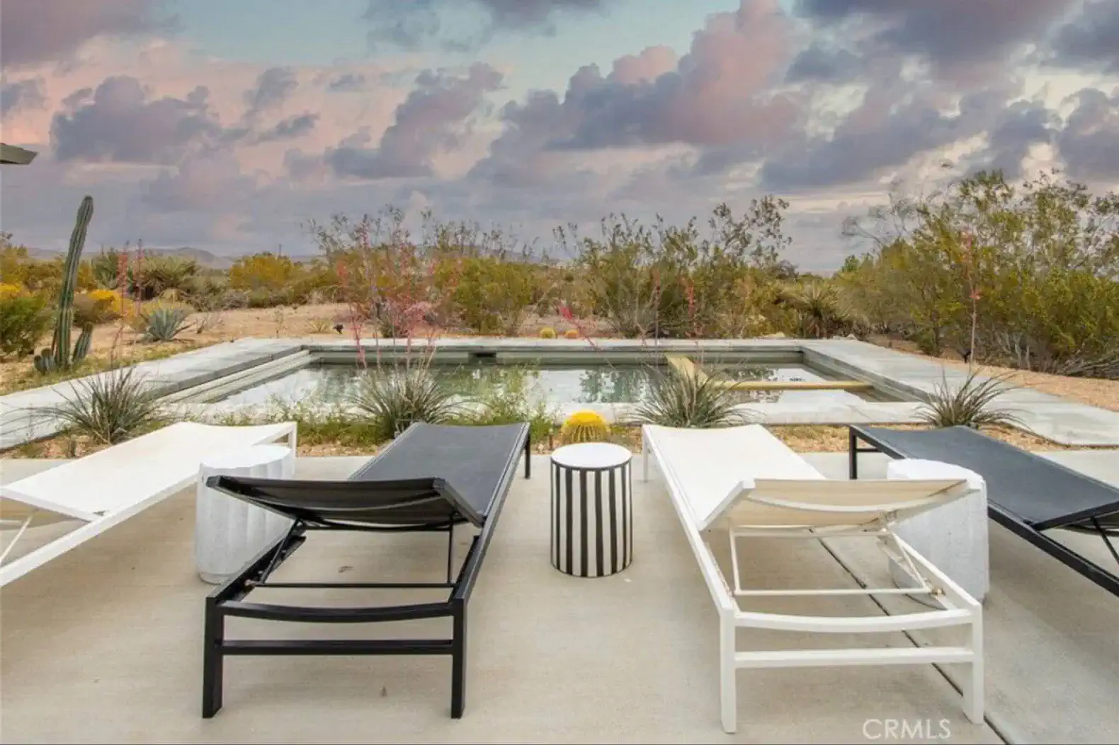 Lounge chairs by a pool with desert landscape and colorful sky