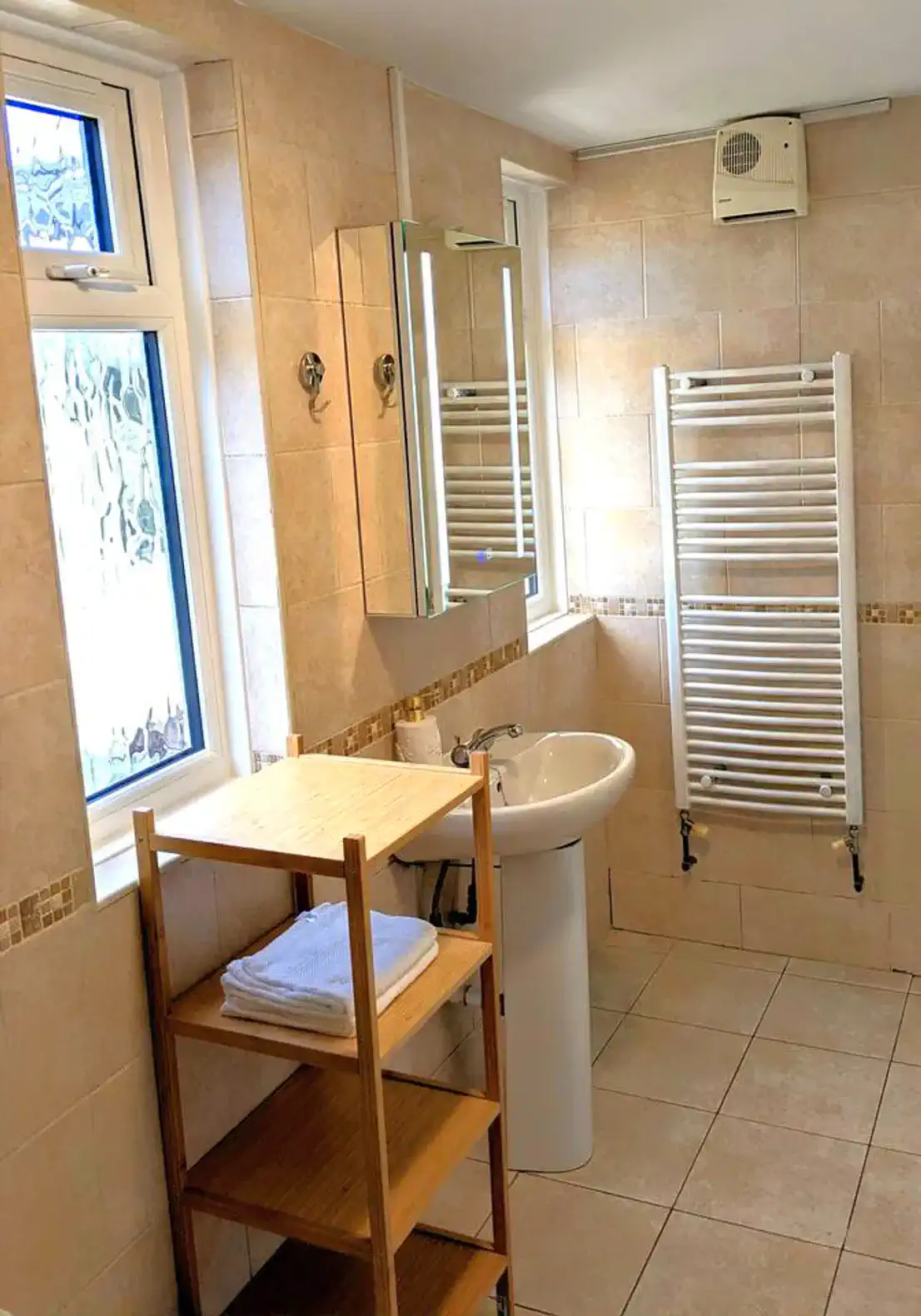 Bright bathroom with tiled walls, sink, LED mirror, and towel rack
