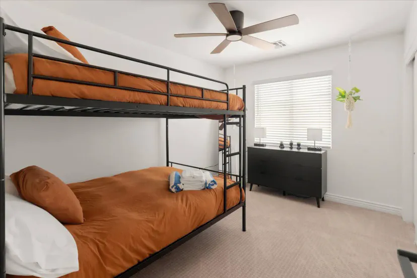 Cozy bunk room with orange bedding and a dresser, featuring a ceiling fan and natural light