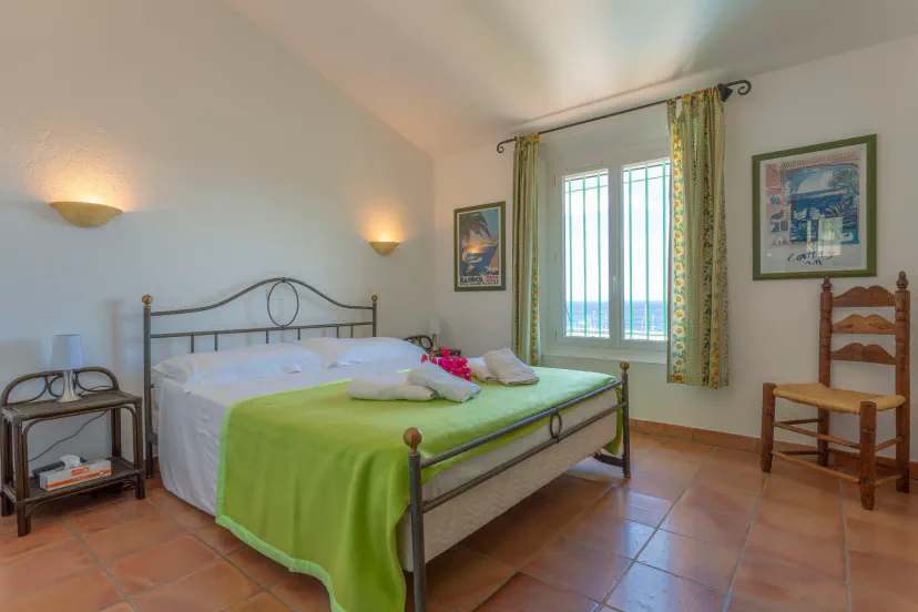 Bright bedroom with a double bed, green bedding, and a window offering sea views, complemented by decorative artwork and rust
