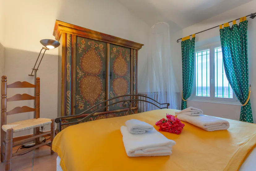 Bright bedroom with a yellow bedspread, decorative wardrobe, and colorful curtains overlooking the sea