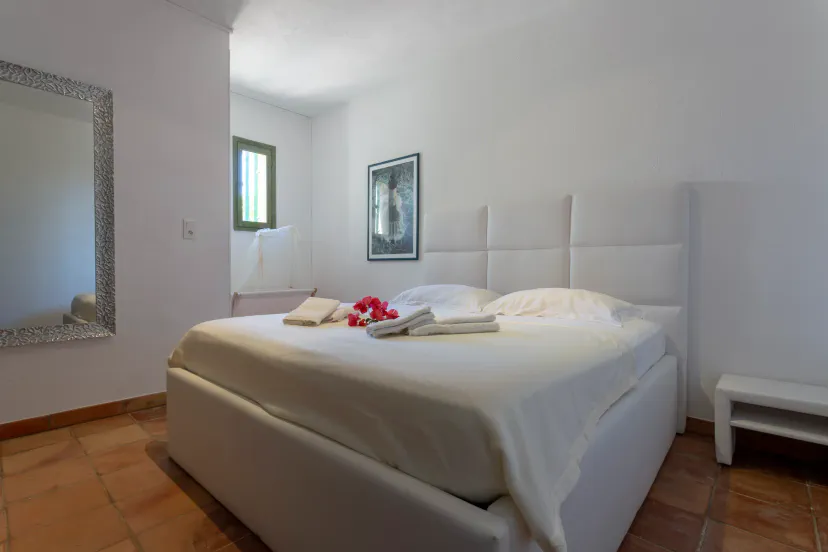 Spacious bedroom with a large white bed, decorative mirror, and soft natural light streaming in