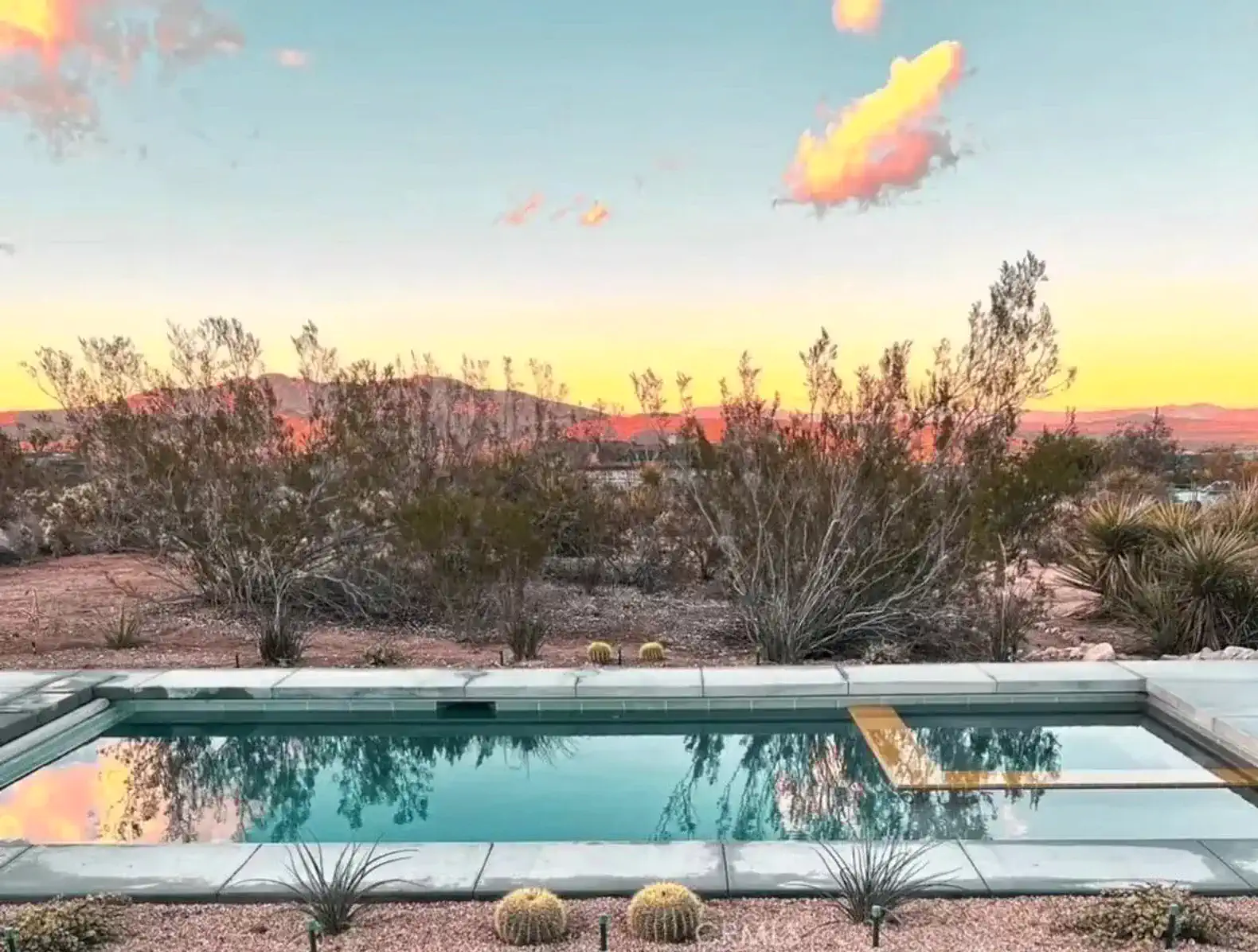 Serene pool reflecting the colorful sunset with desert landscape in the background