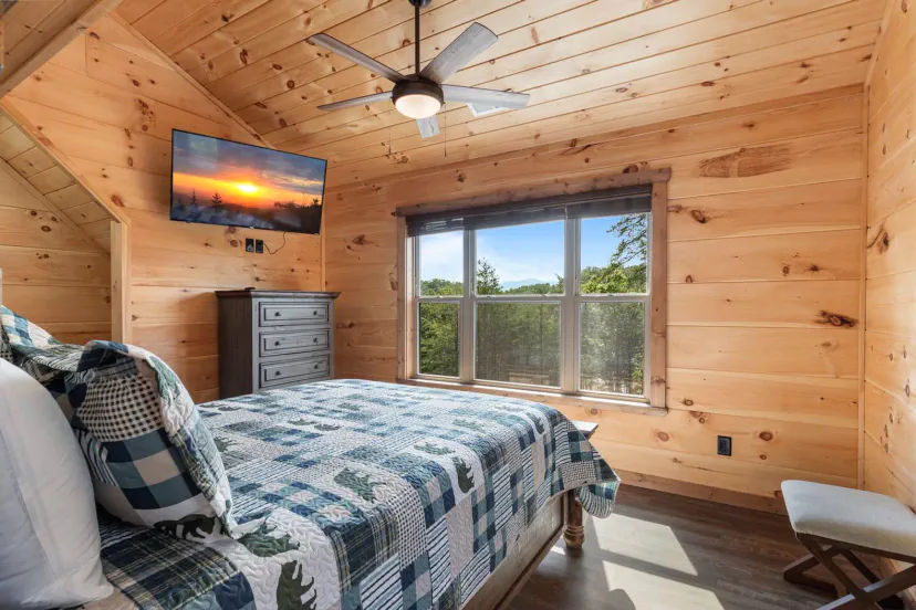 Cozy bedroom with wooden walls, a quilted bed, and a scenic view from the window