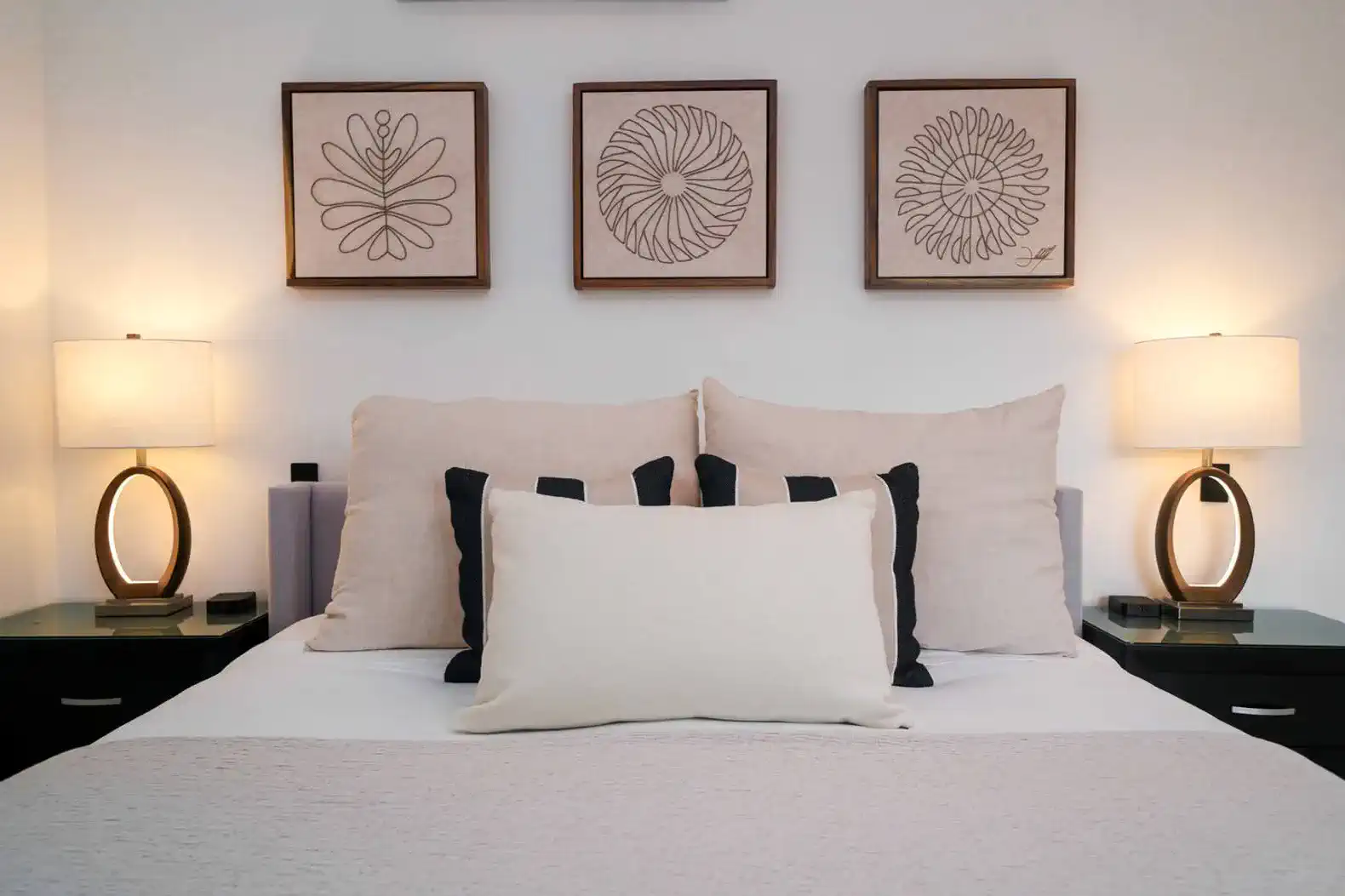 Cama con almohadas decorativas y lámparas de noche en un ambiente acogedor