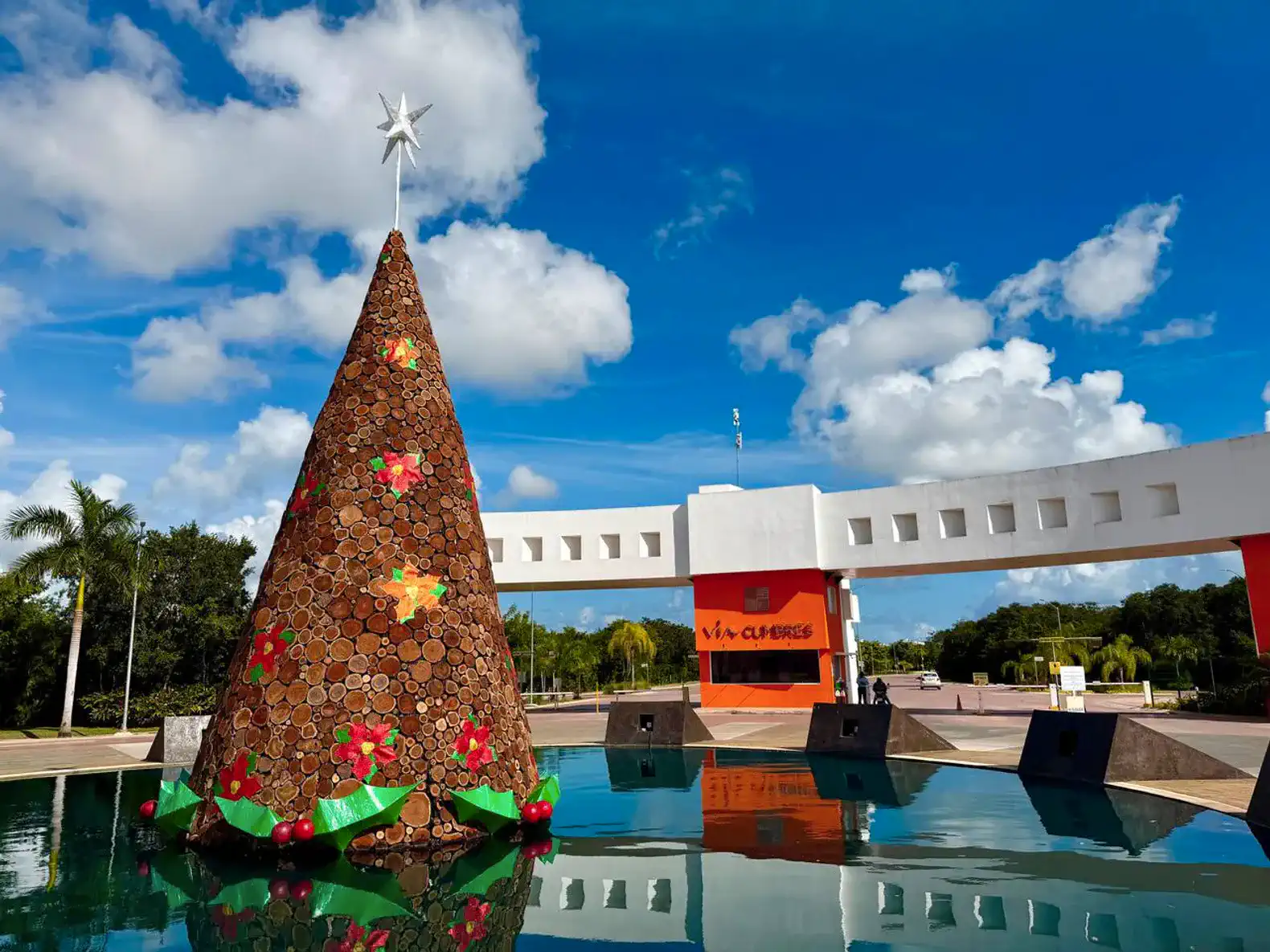 Árbol de Navidad decorado frente a una entrada con agua reflejante y cielo azul