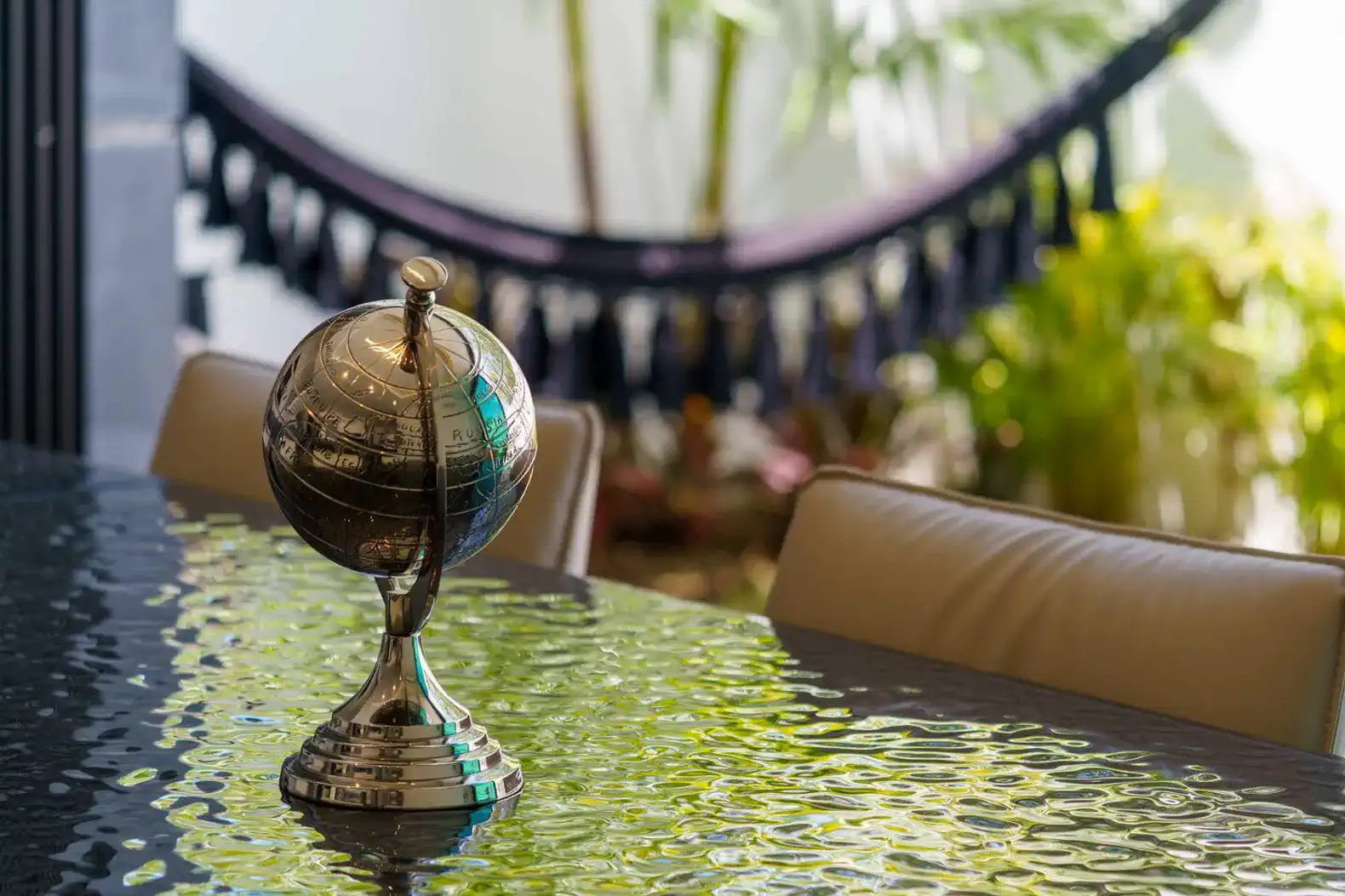 Globo terráqueo decorativo sobre mesa de comedor con fondo de plantas y hamaca