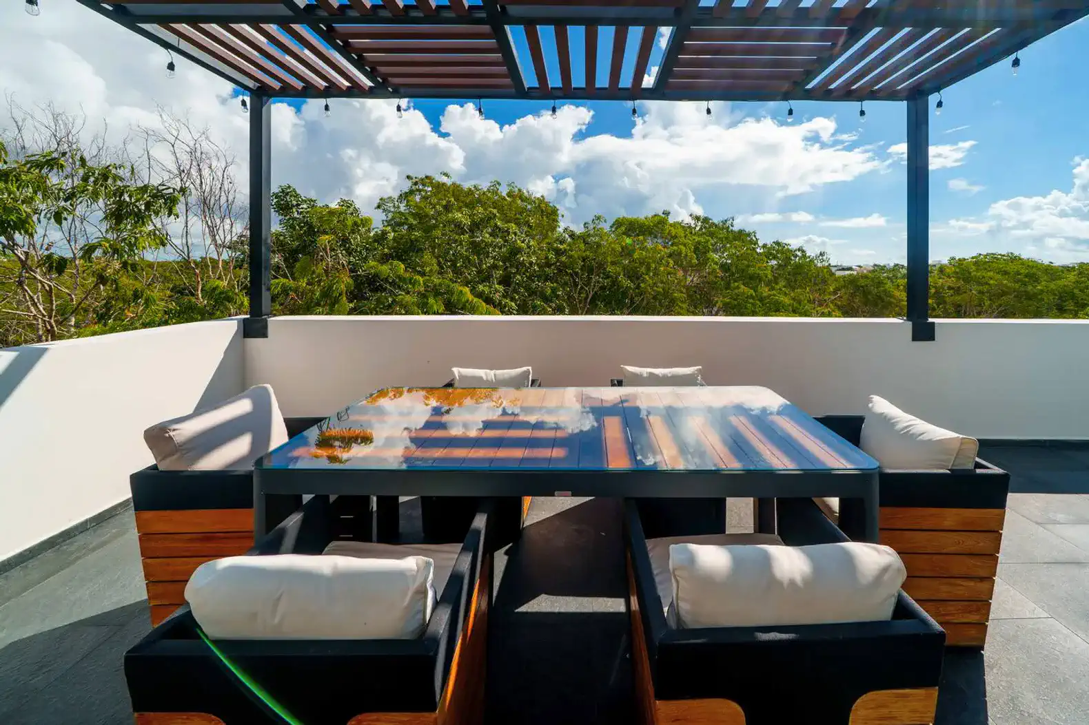 Terraza con mesa de comedor y sillas, rodeada de vegetación y cielo despejado