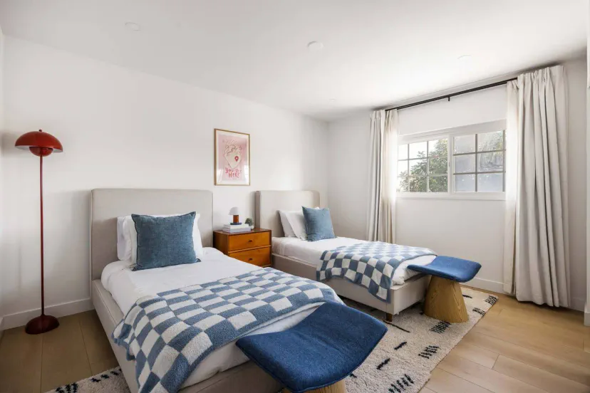 Bright guest bedroom with two twin beds, blue accents, and natural light