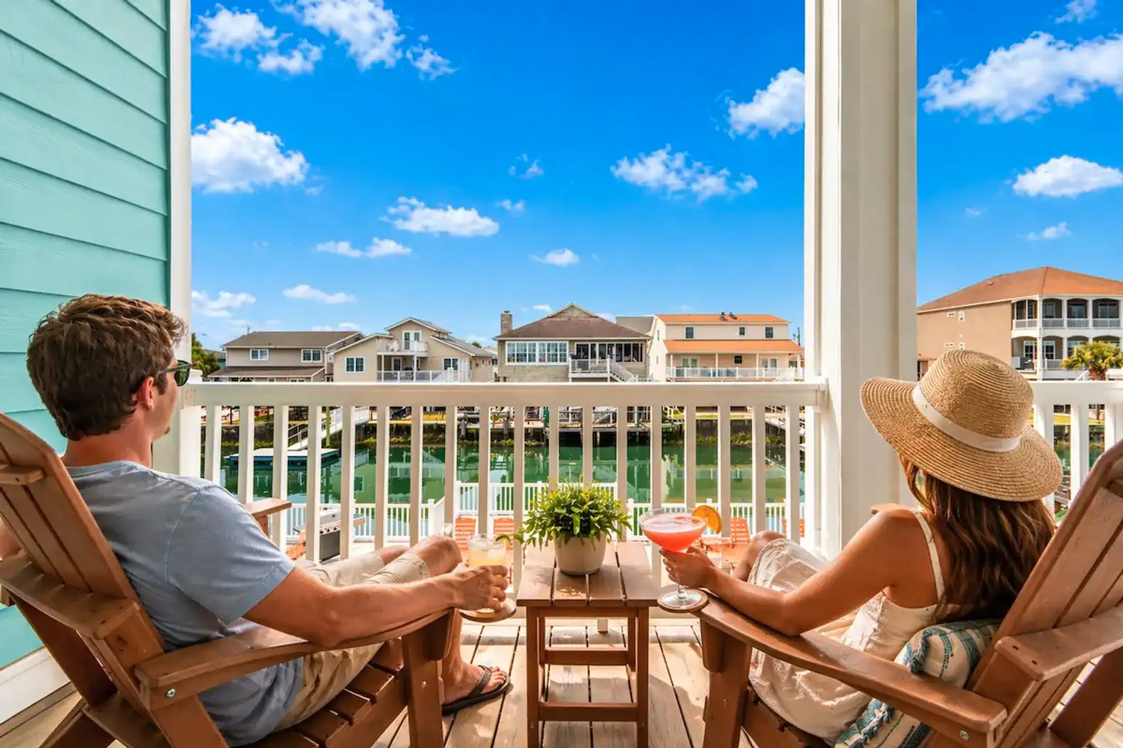 Couple enjoying drinks on a balcony overlooking the water and nearby houses