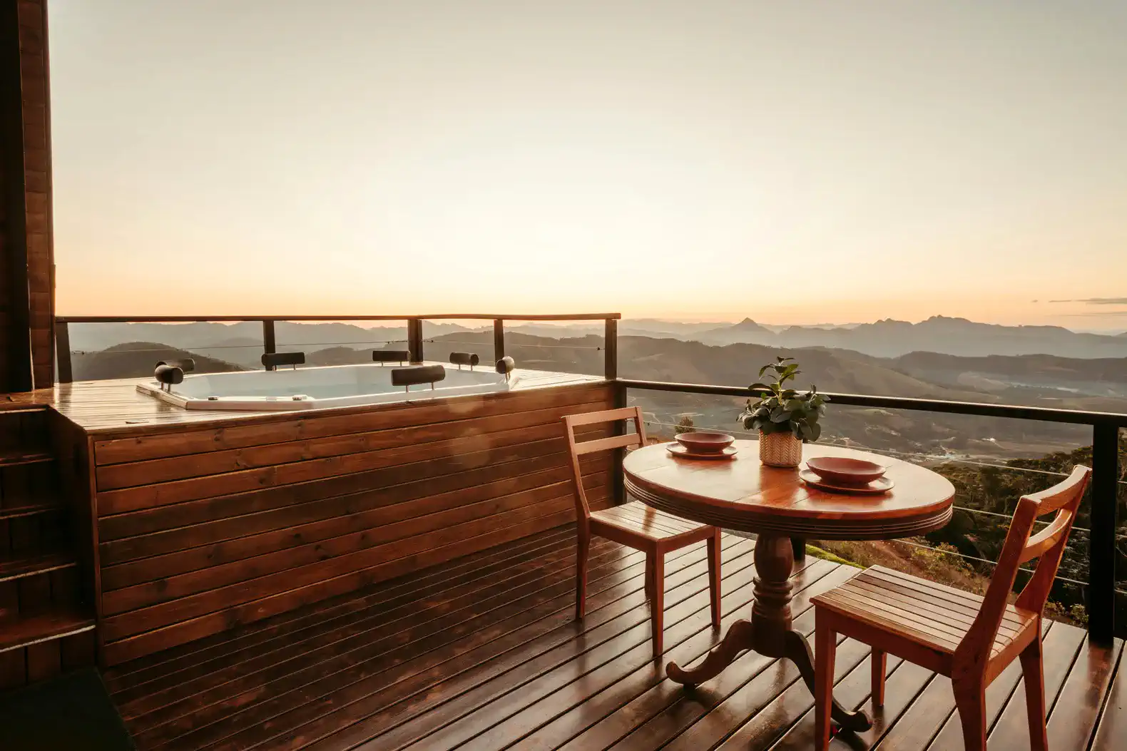 Wooden deck with a hot tub and a dining table overlooking a scenic sunset view