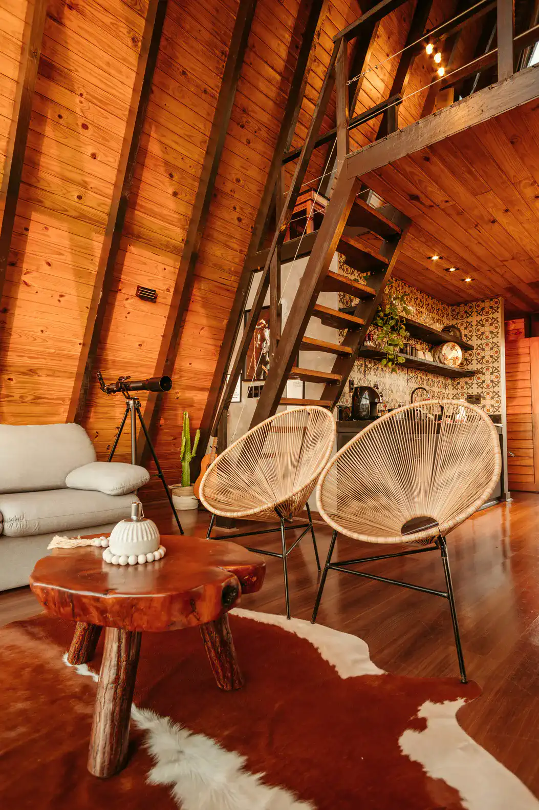 Cozy living area with wooden beams, unique chairs, and a staircase leading to a loft
