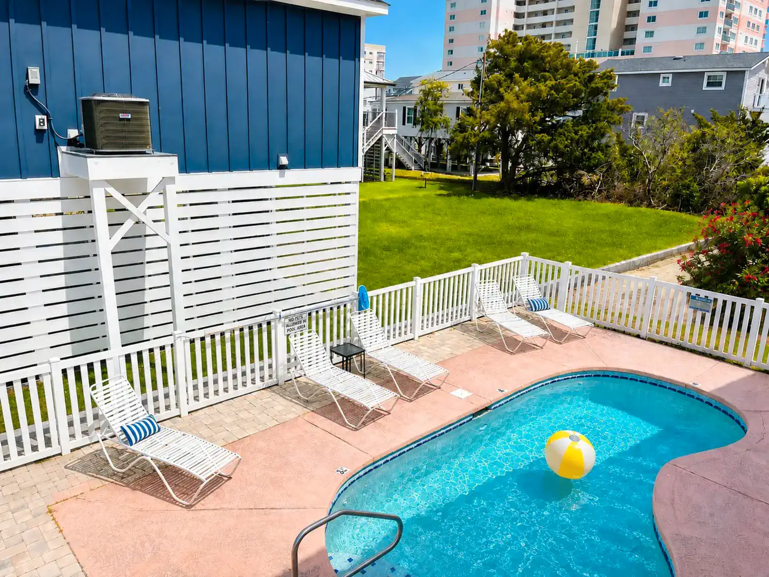 Inviting pool area with lounge chairs and a beach ball, surrounded by a white fence