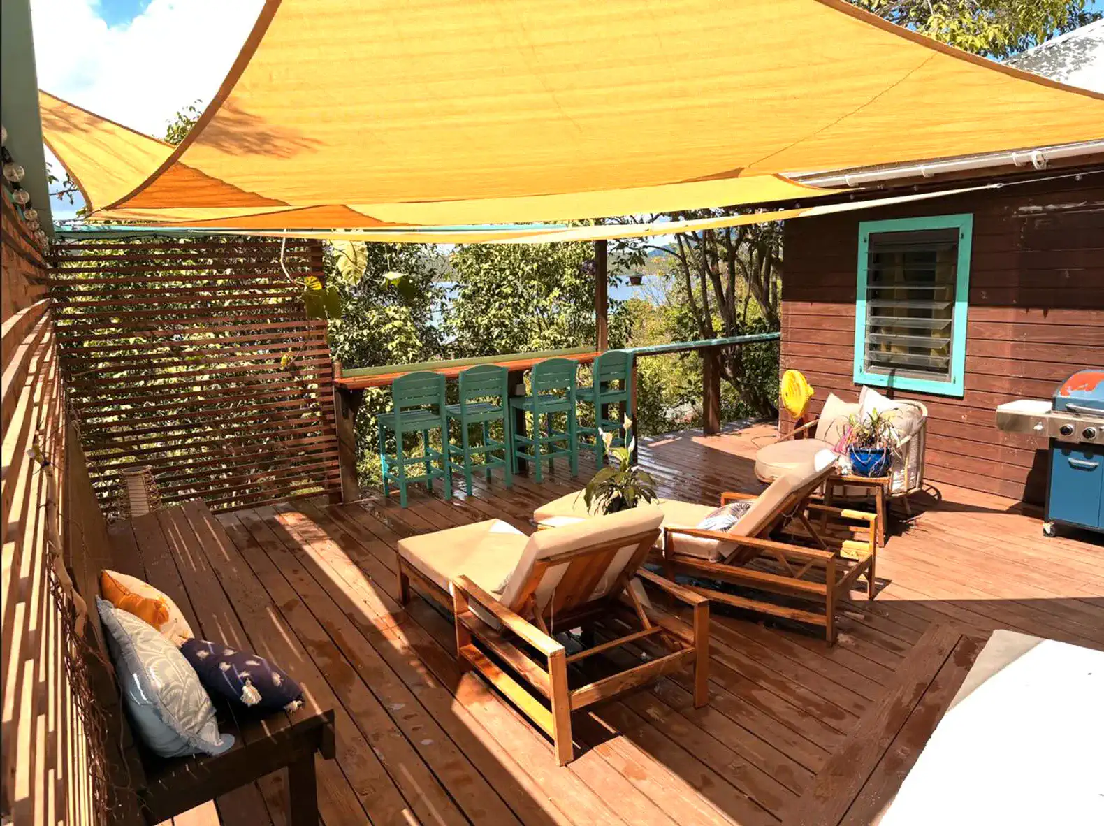 Spacious outdoor deck with loungers, dining area, and a grill under a yellow shade