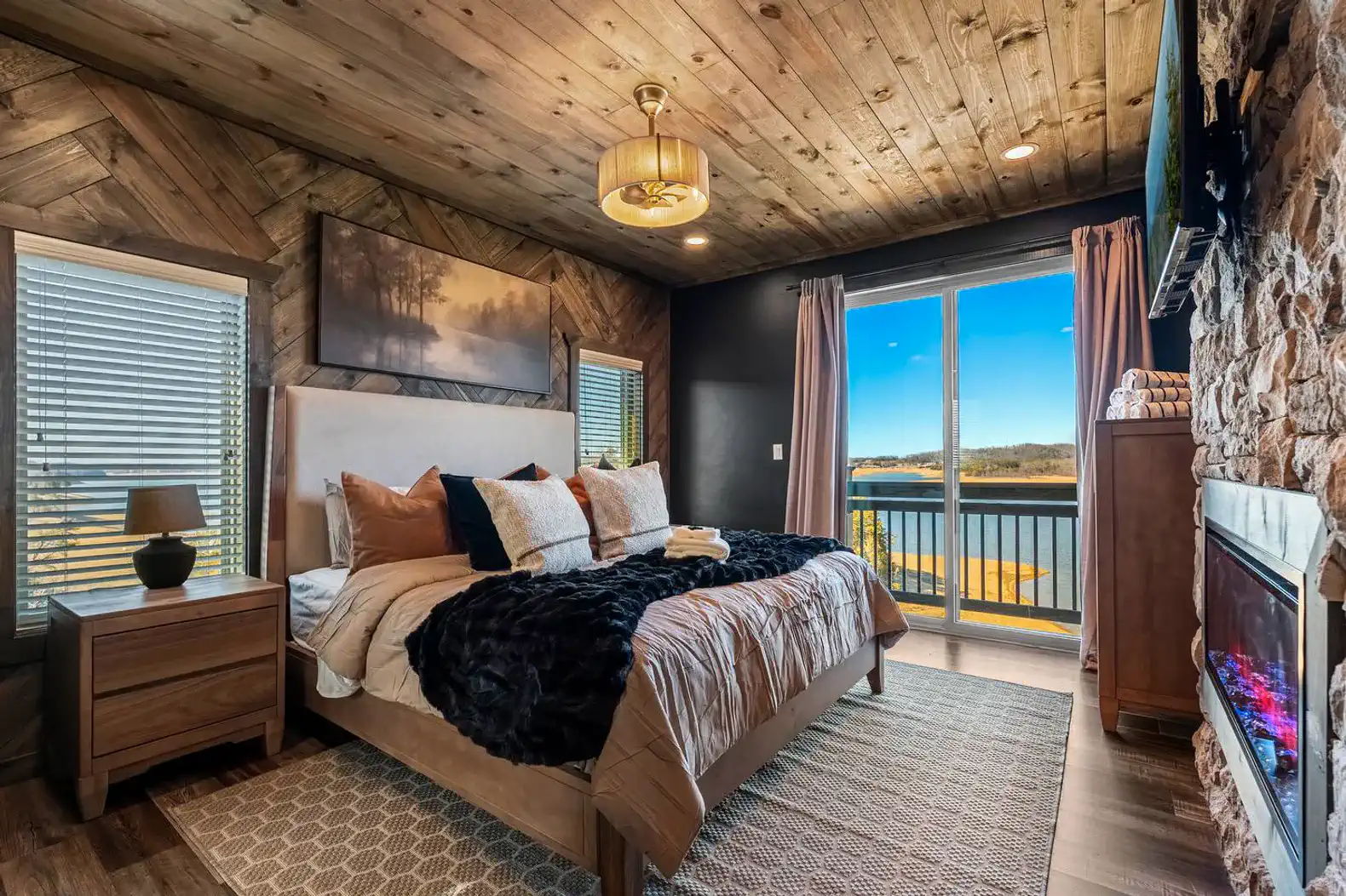 Cozy master bedroom with lake views, large windows, and a stone fireplace