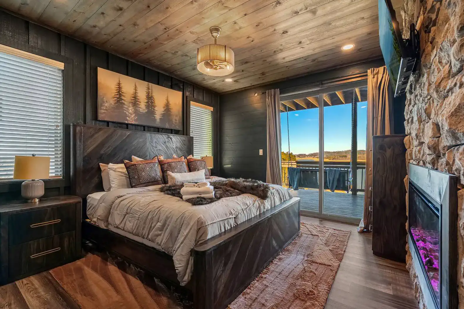Cozy master bedroom with lake views, stone fireplace, and sliding doors to a deck