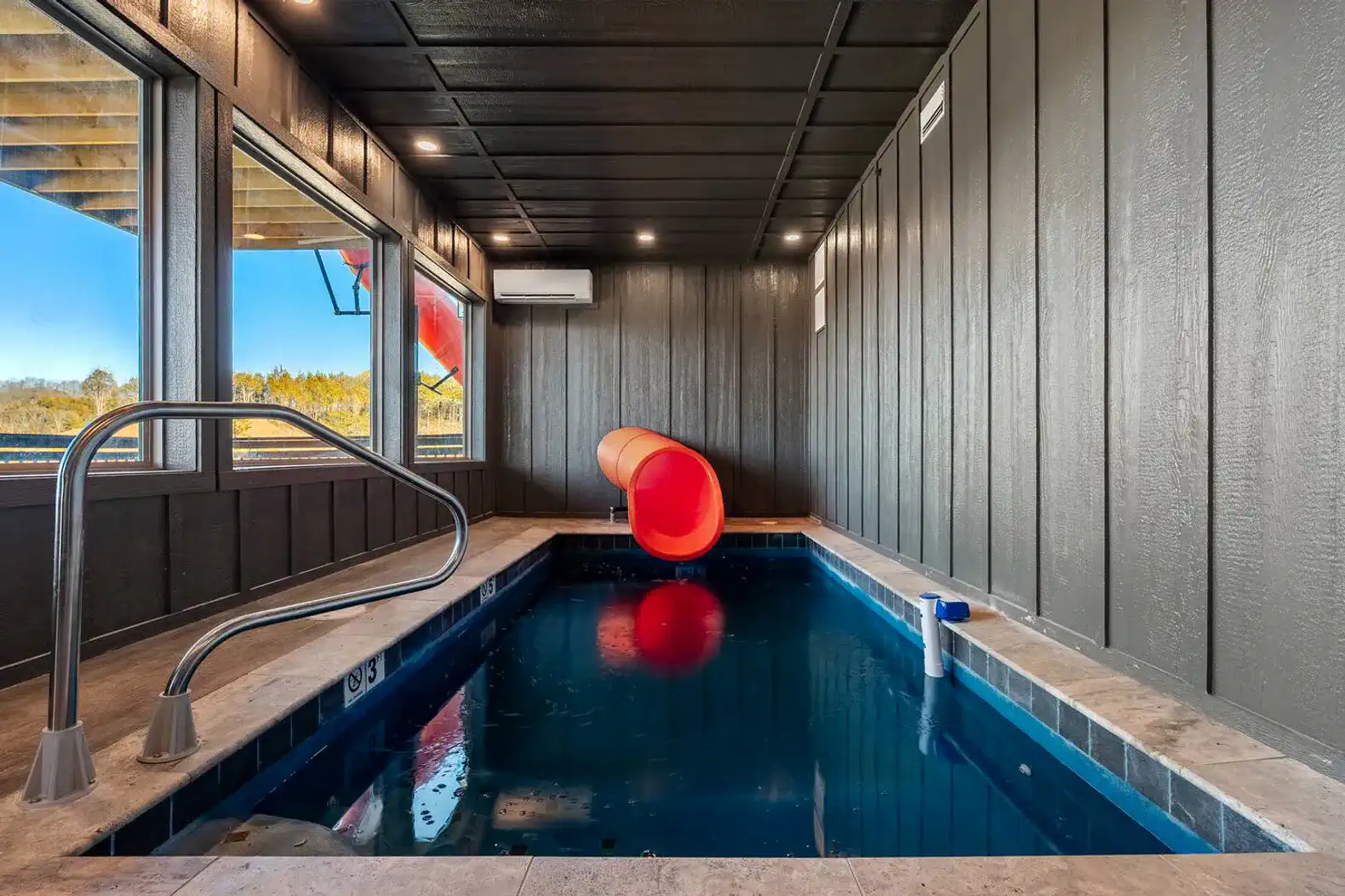 Indoor pool with a water slide and large windows overlooking the lake
