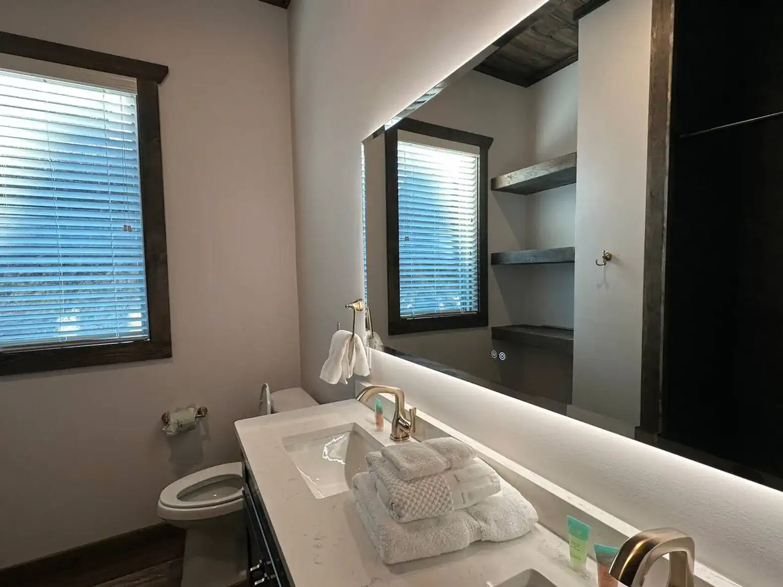 Modern bathroom with a large mirror, shelves, and neatly arranged towels