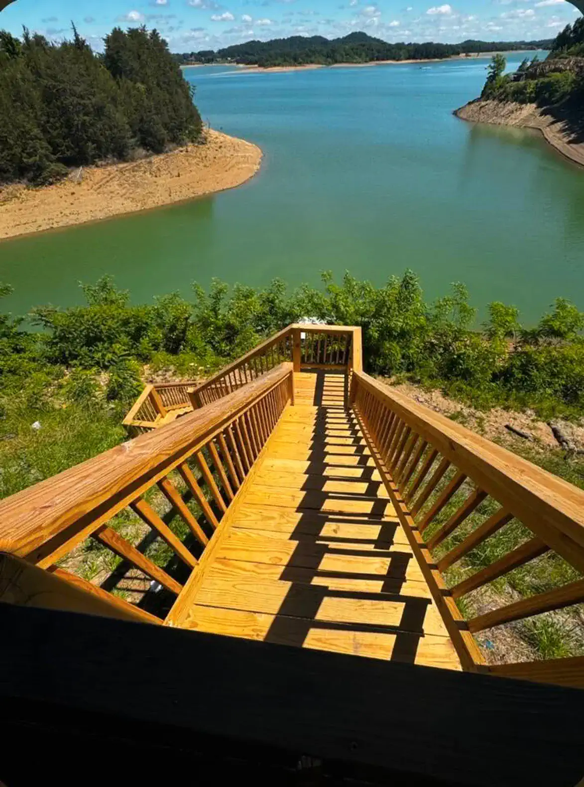 Wooden stairs leading down to a serene lake with green waters and surrounding trees