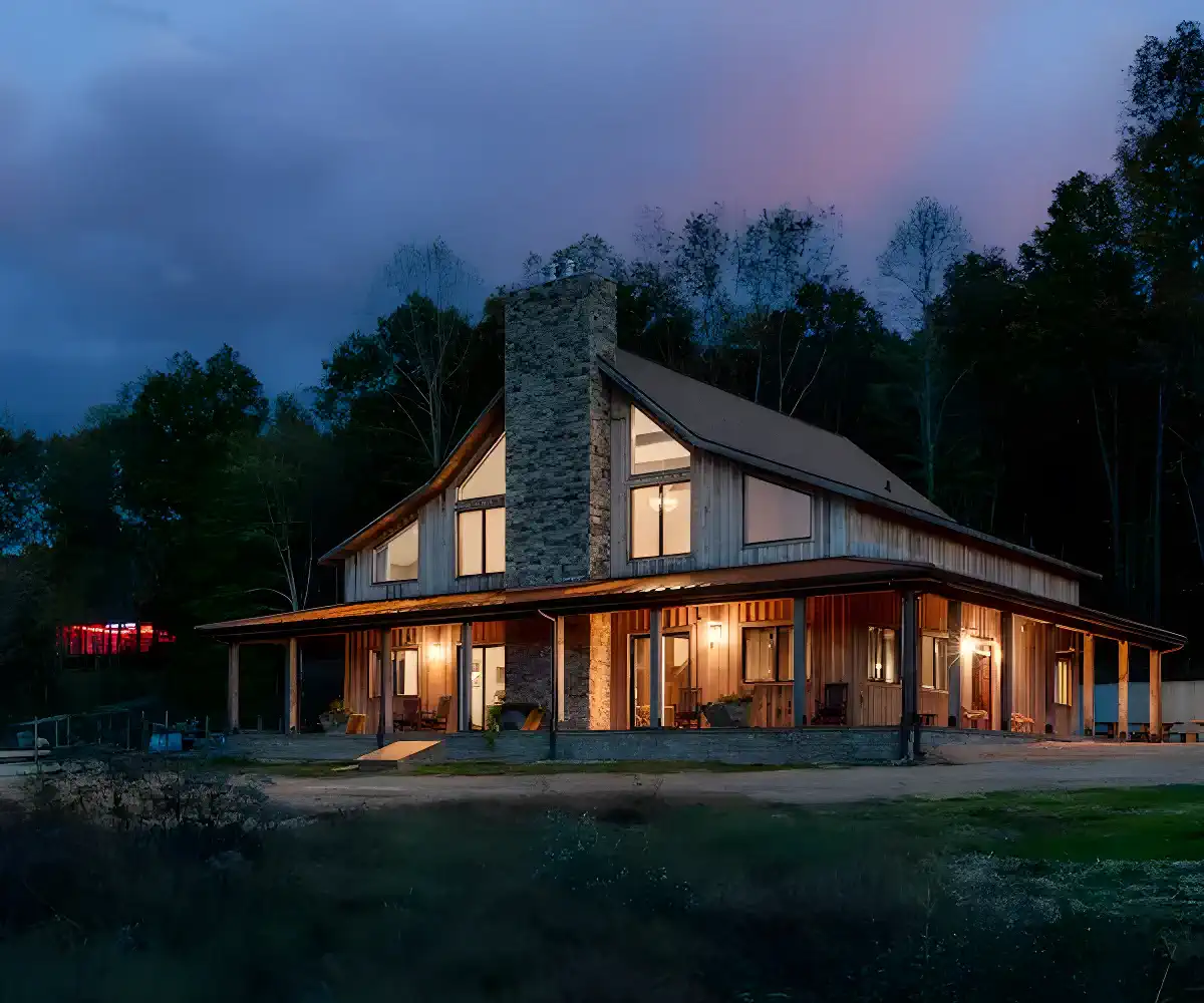 Charming exterior of a rustic cabin with a stone chimney and large windows at dusk