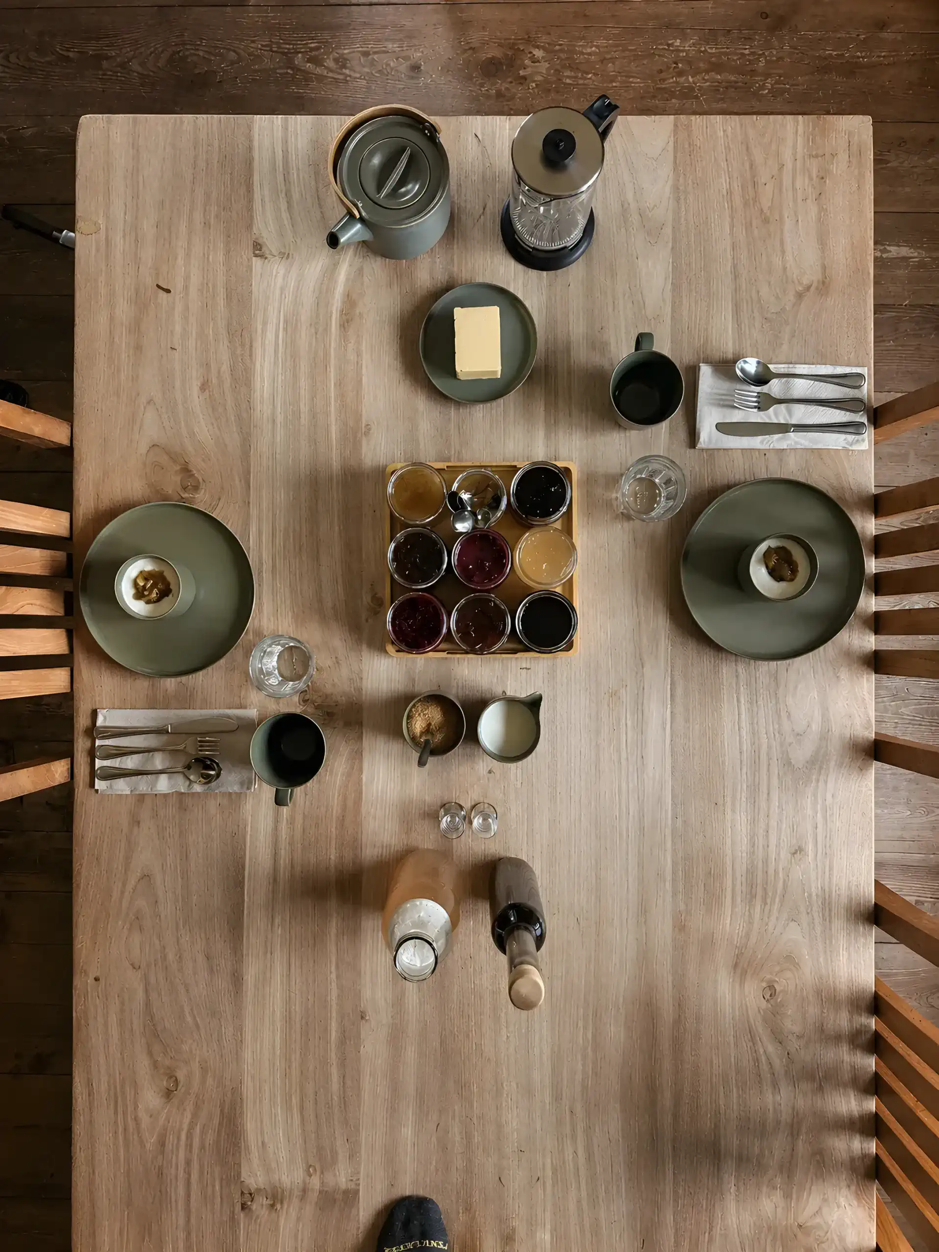 Une table à manger en bois dressée avec des articles pour le petit-déjeuner, y compris du café, du beurre et diverses confitures.